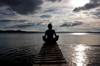 Person meditating at the end of a dock on the ocean